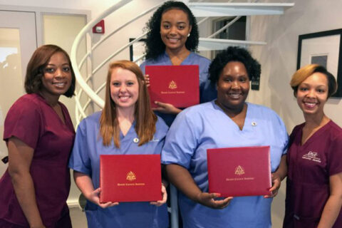 Group of individuals in medical scrubs holding red certificates in front of a spiral staircase