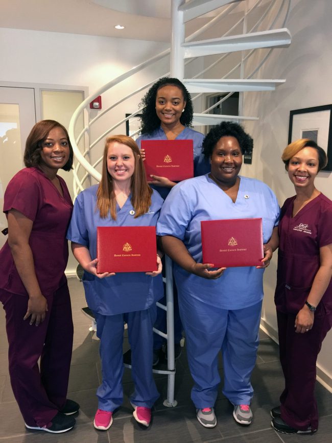 Group of individuals in medical scrubs holding red certificates in front of a spiral staircase