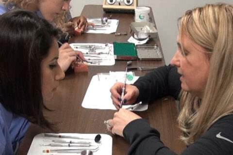 Students practicing dental instrument techniques at a table.