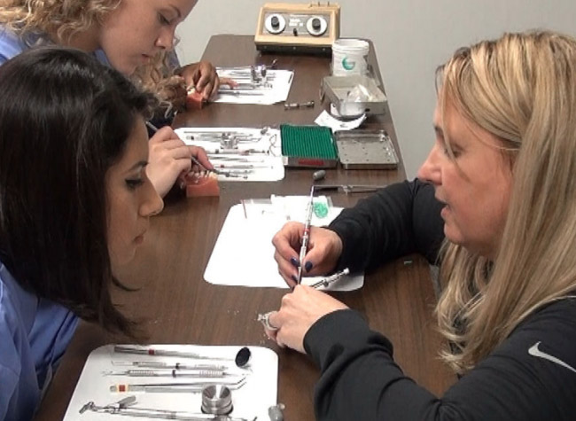Students practicing dental instrument techniques at a table.
